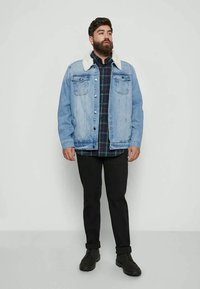 Jaqueta de ganga azul claro com gola de pelagem sintética, camisa xadrez preta e verde por baixo, calças pretas e botas pretas.