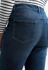 Jeans de mezclilla azul oscuro con una cinturilla alta, que cuentan con dos bolsillos traseros y una textura suave. Acompañados de una camiseta de manga larga a rayas en blanco y negro.