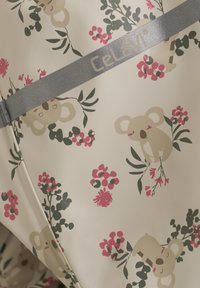 Lysfarvet stof med et koala- og blomsterdesign i pink og grøn. Et sølvbånd med "Celavi"-branding er synligt.