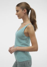 Lichtblauw gebreid mouwloos topje met een V-hals, met een gestructureerd oppervlak en een smalle pasvorm. Gecombineerd met lichtgrijze jeans.