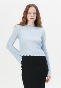 Light blue ribbed long-sleeve top with a scalloped hem, worn with a black ribbed skirt, featuring a fitted design and smooth texture.
