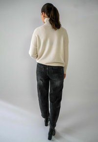 Ivory gebreide trui met hoge kraag, gecombineerd met donkerblauwe jeans en zwarte enkellaarsjes met hak. Eenvoudig, ontspannen pasvorm ontwerp, textiel met structuur.