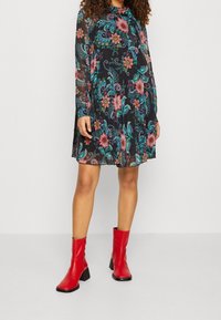 Blommig klänning med svart bakgrund, långa genomskinliga ärmar och löst snitt. Matcher med röda ankelstövlar med fyrkantig tå.