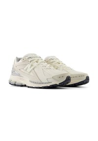 Pair of off-white New Balance running shoes with mesh and suede details, chunky soles, and logo on sides and tongues.