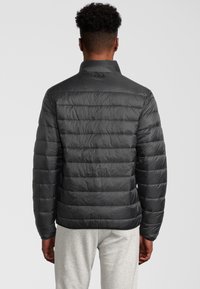 Svart puffjacka med horisontell quiltad design, hög krage och logodetalj på baksidan. Mjuk, något glansig textur.