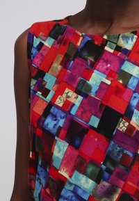 Mehrfarbiges ärmelloses Oberteil mit einem Patchwork-Design aus Quadraten in Rot, Pink, Blau und Schwarz mit einer glatten, weichen Textur.