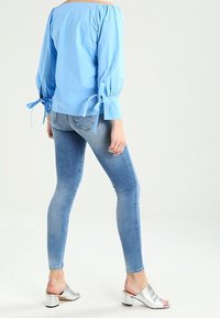 Blusa azzurro chiaro con spalle scoperte, maniche a palloncino e dettaglio con fiocco. Abbinata a jeans aderenti azzurro chiaro e tacchi aperti argento.