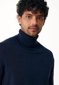 Marineblauer Rollkragenpullover aus glattem Stoff, mit hohem Kragen und taillierter Passform, die einen eleganten und minimalistischen Look betont.