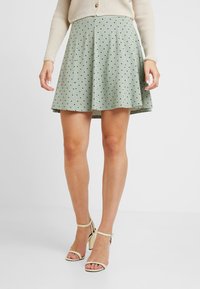 Lichtgroene uitlopende rok van zacht stof met zwarte stippen, met een geplooid ontwerp en een lengte tot halverwege de dij.