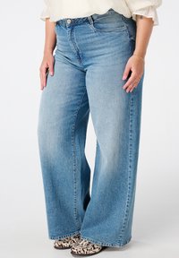 Lichtblauwe jeans met hoge taille en wijde pijpen van denimstof, voorzien van voorzakken en een afgewerkte zoom, gecombineerd met enkellaarsjes met dierenprint.
