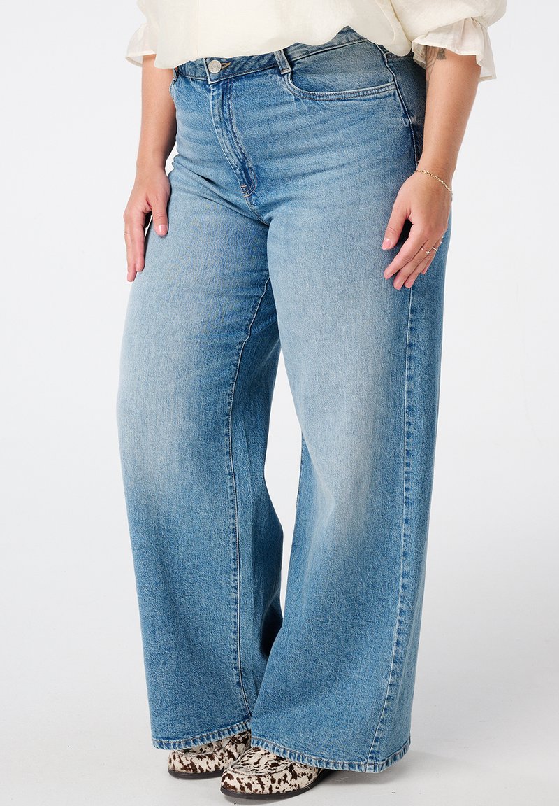 Lichtblauwe jeans met hoge taille en wijde pijpen van denimstof, voorzien van voorzakken en een afgewerkte zoom, gecombineerd met enkellaarsjes met dierenprint.