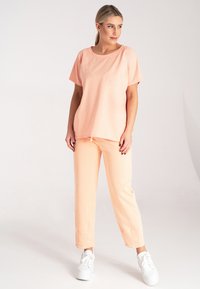 T-shirt w kolorze brzoskwiniowym w luźnym kroju oraz pasujące do niego spodnie, wykonane z miękkiego materiału, z krótkimi rękawami i elastycznym paskiem na sznurki. Białe sneakersy dopełniają całość.