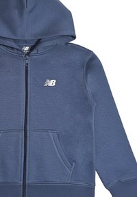 Felpa con cappuccio blu con zip, realizzata in tessuto morbido, con tasca frontale e logo bianco sul petto. Include un cappuccio e polsini a coste.