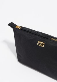 Juodas audinys maišelis su auksine užtrauktuko kilpa ir auksiniu įspaustu logotipu "BIMBA Y LOLA" ant tekstūruoto juodo juostos. Stačiakampio formos, lygaus paviršiaus.