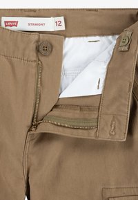 Pantalones rectos de algodón marrón con cremallera, cierre de botón y forro interno blanco. La etiqueta muestra la talla 12.