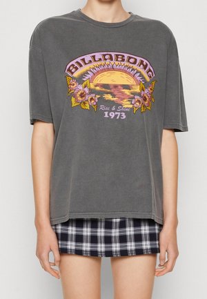 Grå overdimensioneret t-shirt med blomster grafik og solnedgangsdesign i lilla og gul; parret med en sort og hvidternet nederdel.