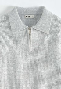 Pull gris à fermeture éclair avec un tricot texturé et un col contrastant gris clair. Doté d'une fermeture éclair en métal et d'un design simple et décontracté.