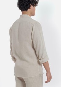 Beige linnen overhemd met een casual kraag, opgerolde mouwen en een comfortabele pasvorm, met een eenvoudige textuur en een rugplooi detail.