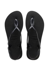 Juodos flip-flop šlepetės su tekstūruotais guminiais padais ir nupintas dirželis. Dirželiai yra išnagrinėti ir pritvirtinti prie pado apvaliais jungiamaisiais detalėmis.