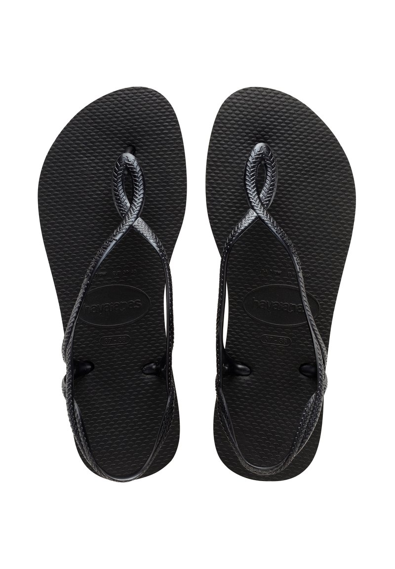 Juodos flip-flop šlepetės su tekstūruotais guminiais padais ir nupintas dirželis. Dirželiai yra išnagrinėti ir pritvirtinti prie pado apvaliais jungiamaisiais detalėmis.