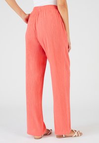 Pantalons plissés de couleur pêche avec une taille élastique. Coupe ample et jambes droites, associés à de simples sandales plates, mettant l'accent sur le confort et le mouvement.