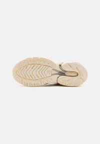 Suola di una sneaker in un beige chiaro con un motivo di battistrada testurizzato, caratterizzata da una sezione centrale liscia e un sottile dettaglio di branding.