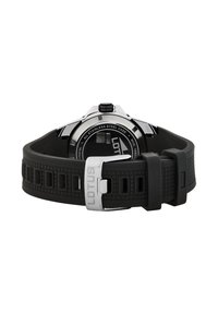 Svart gummiklockarmband med rektangulära utskärningar, klockhus i rostfritt stål och silverfärgad spänne. Cirkulär urtavla med svart skiva och vita markeringar.