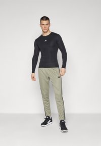 Zwart langetijd sportshirt, slim fit, met wit logo; olijfgroene joggingbroek met zijstripes; zwarte sportschoenen.