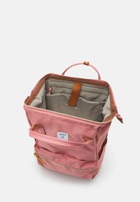 Sac à dos en tissu rose avec une fermeture éclair, des accents beige et une poignée supérieure. L'intérieur spacieux comprend plusieurs poches et une doublure de couleur claire.