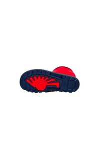Semelle en caoutchouc avec des détails rouges, présentant un motif de grip texturé. Le fond bleu contraste avec la partie supérieure de la chaussure.