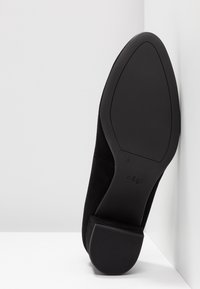 Chaussure à talon haut en daim noir avec un bout pointu et une semelle en caoutchouc texturée. Marque visible sur le côté intérieur de la semelle.