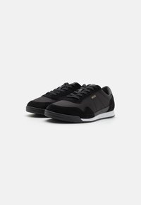 Svart sneakers med en blanding av glatt skinn og semsket skinn, med teksturerte detaljer og en hvit gummisole. Logo synlig på siden.