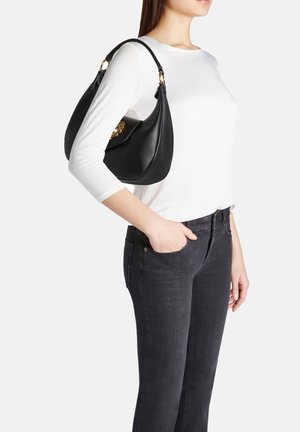 Borsa a tracolla in pelle nera con una forma curva, superficie testurizzata, dettagli in metallo dorato e una larga tracolla, indossata di lato.