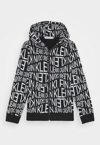 Felpa con zip nera caratterizzata da un motivo di testo bianco ripetuto "CALVIN KLEIN JEANS". Realizzata in tessuto morbido con una tasca frontale e cappuccio.