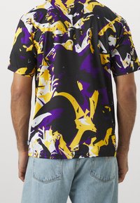 Kortärmad t-shirt i svart med stora lila och gula abstrakta mönster, med en avslappnad passform och mjuk textur.