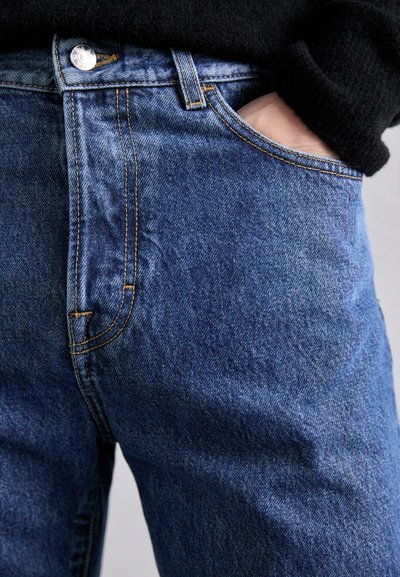 Τζιν παντελόνι σε μεσαία μπλε απόχρωση, με κανονικό σχέδιο 5 τσεπών, χάλκινη ραφή και κουμπί στη μέση.