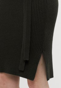 Strikket, mørkegrønn midiskjørt med ribbet tekstur, sideskår og en knyte-detajl i livet. Mykt stoff med en tettsittende design.
