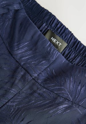 Tessuto blu navy con un sottile motivo a foglia, caratterizzato da una vita elastica arricciata e un'etichetta nera NEXT attaccata.