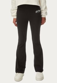 Schwarze, weit geschnittene Jogginghosen aus Baumwollmischung mit weicher Textur und "NEW JERSEY" Druck an der Hüfte. Kombiniert mit weißen Sneakern.