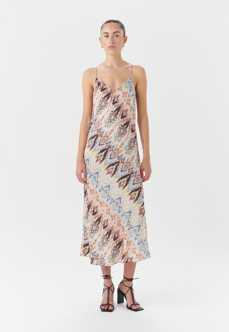 Satin midi suknelė su V formos iškirpte ir plonomis petnešėlėmis, turinti spalvingą abstrakčią modelį oranžinės, mėlynos ir geltonos spalvų. Juodos blokinės pirštinės sandalai.