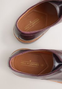 Chaussures en cuir de couleur bordeaux foncé, texture lisse, détails cousus et un logo doré sur la doublure intérieure.