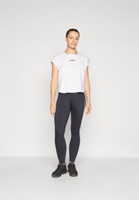 White cropped t-shirt with "STRONGER" text, paired with high-waisted black leggings featuring white side stripes. Black athletic shoes.