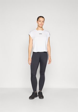 Weißes, kurzes T-Shirt mit dem Text "STRONGER", kombiniert mit hoch taillierten schwarzen Leggings mit weißen Seitenstreifen. Schwarze Sportschuhe.