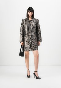 Blazer med et metallisk zebra mønster, med en strukturert silhuett, dobbelspent front, kombinert med et matchende skjørt og svarte tilbehør.