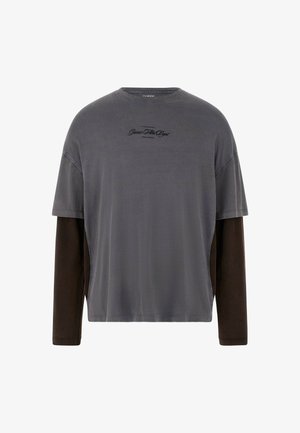 Siva majica s kratkimi rokavi in dolgimi rjavimi rokavi, narejena iz mehkega materiala. Vsebuje subtilen črn logotip na prsih in detajle na stranskem delu.