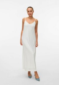 Witte maxi-jurk met een V-hals en dunne bandjes, met een zigzagpatroon en een gladde textuur, gecombineerd met puntige blauwe hakken.