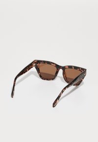 Óculos de sol em padrão tartaruga com um design de olhos de gato, lentes castanhas e armações de plástico lisas com um destaque metálico nas hastes.