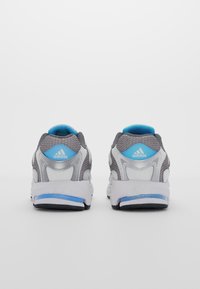 Grå och vita sportskor med blå detaljer, som har en texturerad mesh-ovandel, vadderad krage och en kontrasterande gummisula.