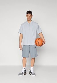 Helehall halli sportlik särk, millel on tõmblukuga krae, sobivate lühikeste pükstega; hoiab korvpalli; hallid tennised mustade detailidega.