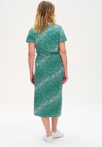 Green dress with white heart pattern, short sleeves, fitted waist, mid-length, made of soft fabric, paired with white sneakers for a casual look.